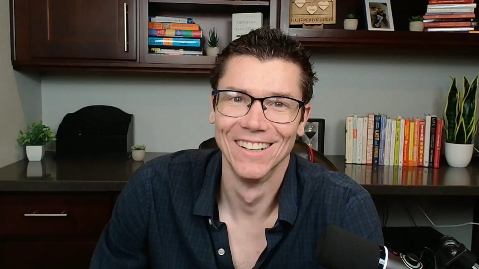 TJ Robertson smiling at his desk in front of bookshelves
